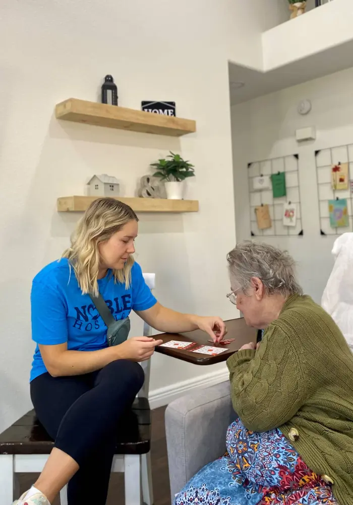 A Noble Hospice volunteer playing a board game with a senior woman patient in her room.