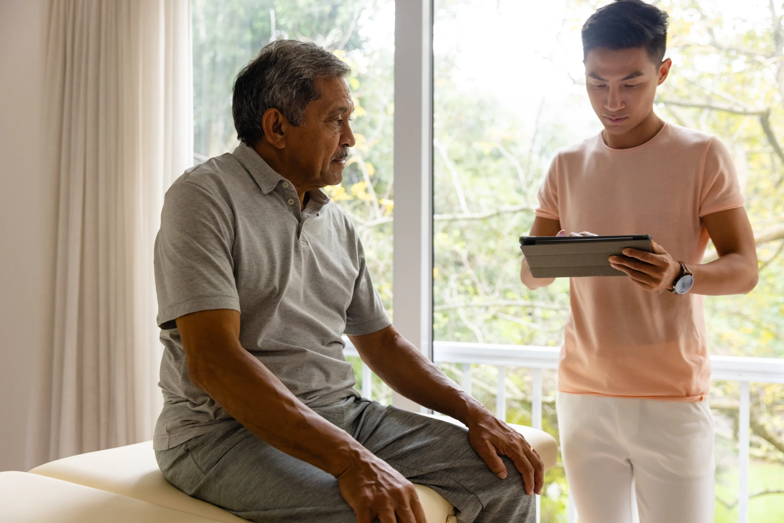 A therapist reviewing a patient’s documentation on a tablet while the patient sits on the side of the bed.